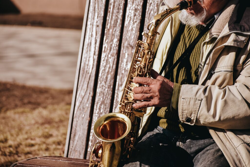 A senior adult playing the saxophone on a park bench, enjoying music outdoors.